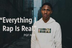 Stylized promotional image of PGF Nuk in a cartoon-print jacket, overlaid with the quote “Everything I Rap Is Real,” set against a dark, gritty Chicago alley for dramatic effect