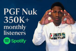 Promotional image of PGF Nuk wearing a white Champion hoodie, with the text “PGF Nuk 350K+ monthly listeners on Spotify” beside him and a Spotify logo on the side, set against a clean background