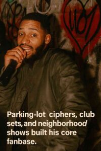 Teejaee holding a microphone while performing against a graffiti-covered wall, with text reading “Parking-lot ciphers, club sets, and neighborhood shows built his core fanbase.”